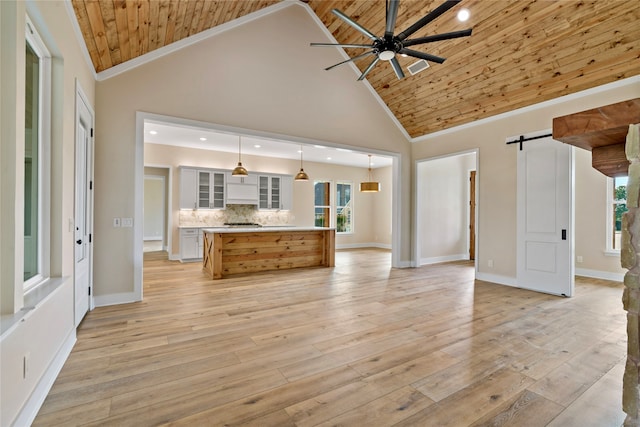 unfurnished living room with plenty of natural light, a barn door, wooden ceiling, and high vaulted ceiling