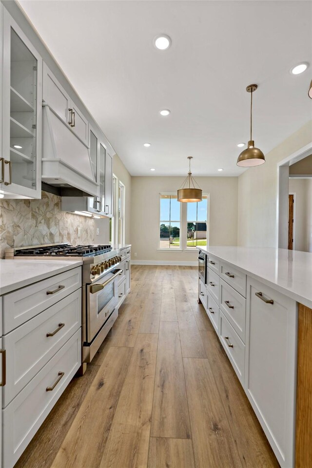 kitchen with high end stove, white cabinetry, hanging light fixtures, and light hardwood / wood-style floors