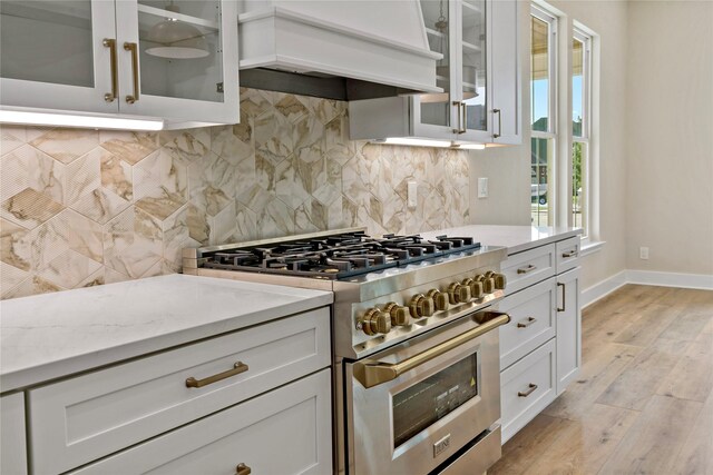 kitchen featuring white cabinets, high end stainless steel range, light hardwood / wood-style flooring, light stone counters, and custom range hood