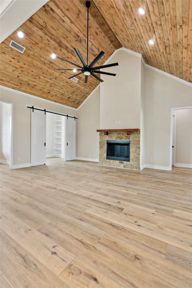 unfurnished living room featuring built in shelves, a barn door, light wood-type flooring, a fireplace, and wood ceiling