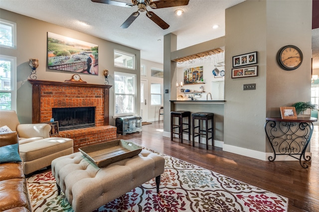 living room featuring ceiling fan, dark hardwood / wood-style flooring, a textured ceiling, and a brick fireplace