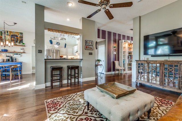 living room featuring ceiling fan with notable chandelier, dark hardwood / wood-style flooring, and a textured ceiling