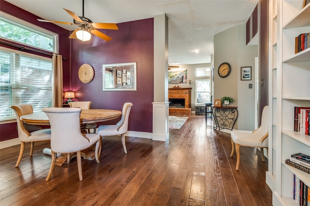 dining room featuring a textured ceiling, plenty of natural light, dark hardwood / wood-style floors, and a brick fireplace