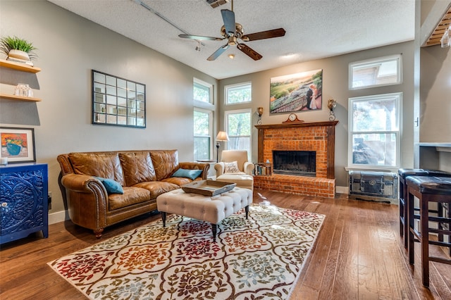 living room with ceiling fan, a fireplace, wood-type flooring, and a textured ceiling