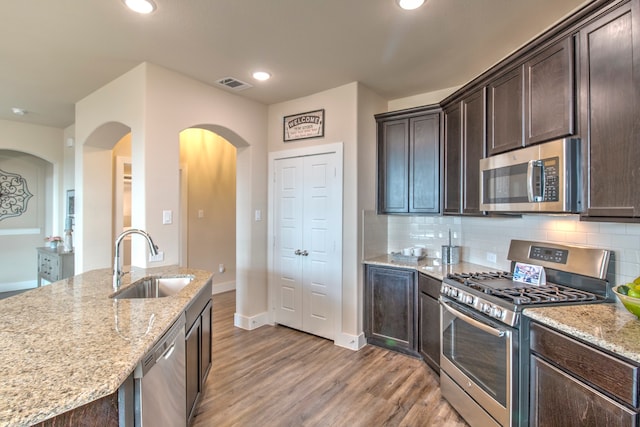 kitchen featuring sink, light wood-type flooring, dark brown cabinets, light stone counters, and stainless steel appliances