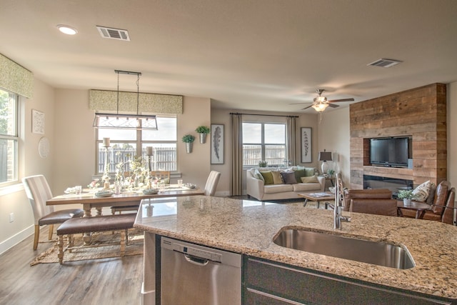 kitchen with light stone countertops, sink, stainless steel dishwasher, hardwood / wood-style floors, and decorative light fixtures