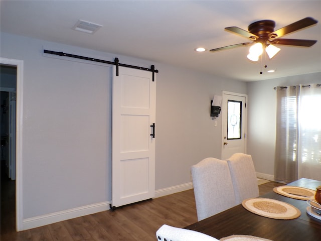 dining area with a barn door, ceiling fan, and dark wood-type flooring