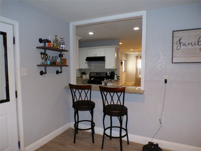 kitchen featuring gas stove, white cabinetry, kitchen peninsula, hardwood / wood-style floors, and a breakfast bar