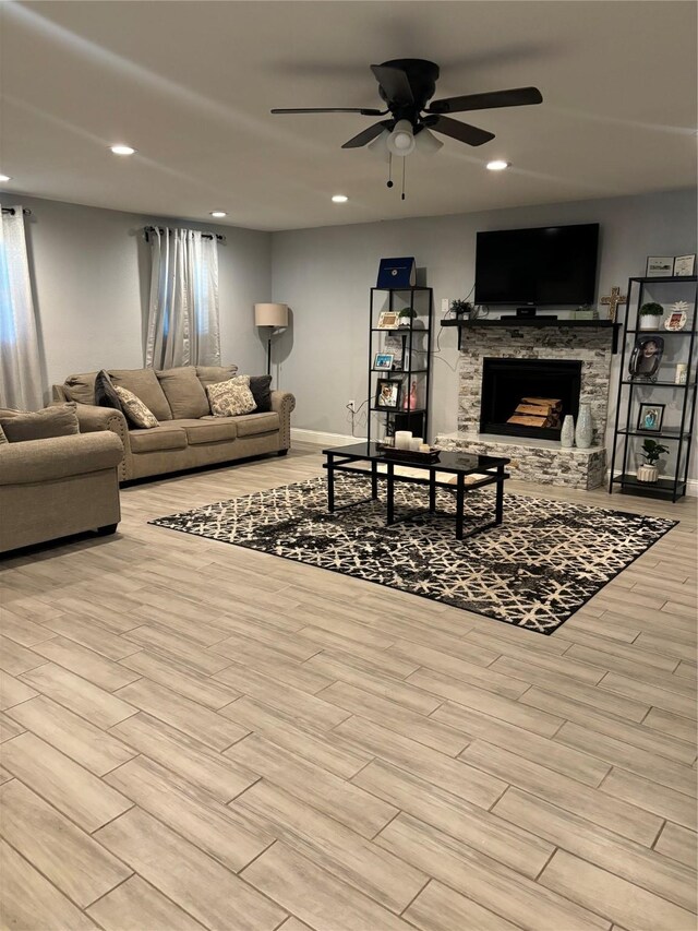 living room with a stone fireplace, ceiling fan, and light hardwood / wood-style floors