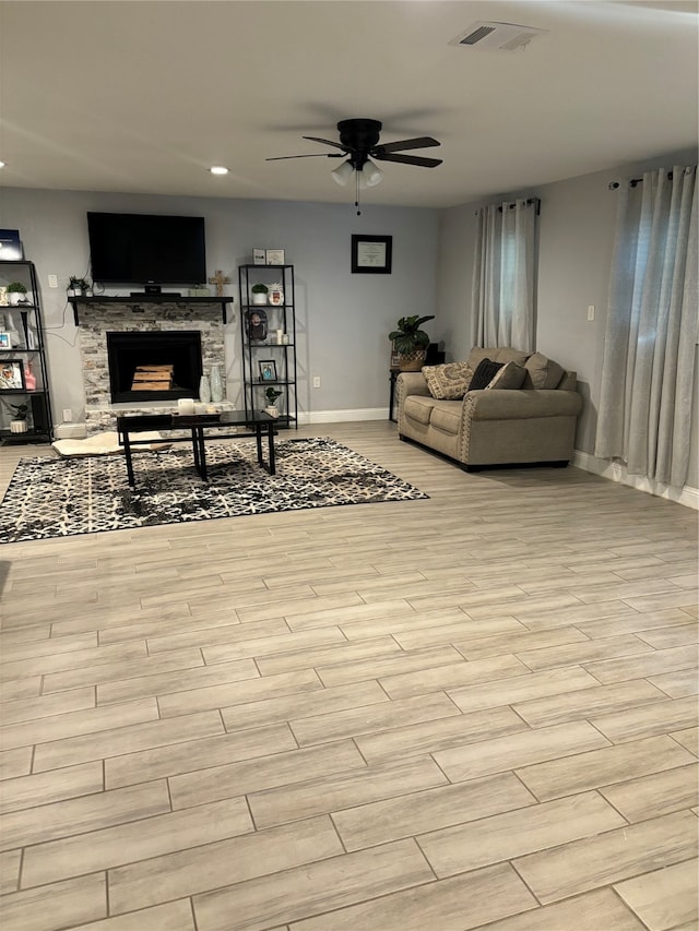 living room featuring light hardwood / wood-style floors, a stone fireplace, and ceiling fan