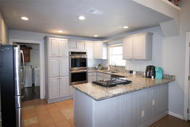 332 NW County Road 2005, Corsicana, TX 75110 - kitchen featuring appliances with stainless steel finishes, washing machine and dryer, a peninsula, a sink, and white cabinetry
