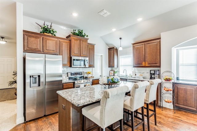 kitchen with light stone countertops, stainless steel appliances, vaulted ceiling, light hardwood / wood-style floors, and a kitchen island