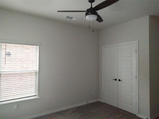 unfurnished bedroom with dark colored carpet, ceiling fan, and a closet