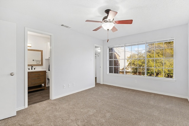 unfurnished bedroom featuring ensuite bathroom, sink, carpet flooring, ceiling fan, and a textured ceiling