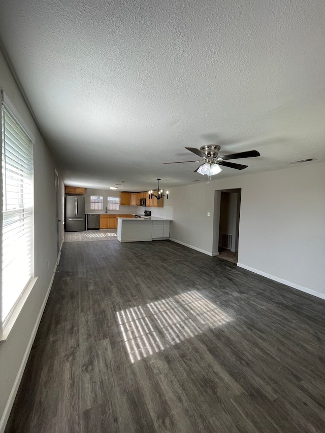 unfurnished living room with ceiling fan with notable chandelier, dark hardwood / wood-style flooring, and a textured ceiling