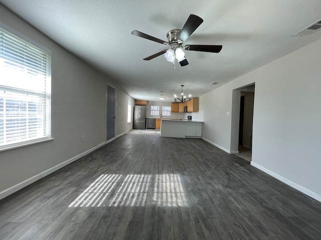 unfurnished living room featuring ceiling fan with notable chandelier, a textured ceiling, and dark wood-type flooring