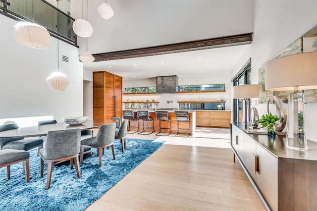 dining space featuring beamed ceiling, a high ceiling, and light hardwood / wood-style flooring