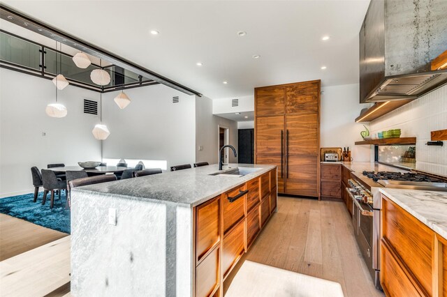 kitchen with double oven range, ventilation hood, a spacious island, sink, and light hardwood / wood-style flooring