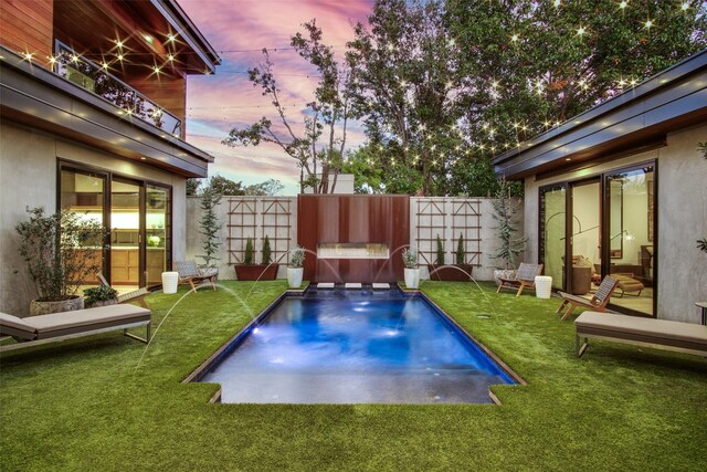 pool at dusk featuring pool water feature and a lawn