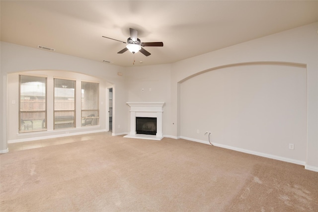 unfurnished living room featuring visible vents, a fireplace with raised hearth, a ceiling fan, baseboards, and light colored carpet