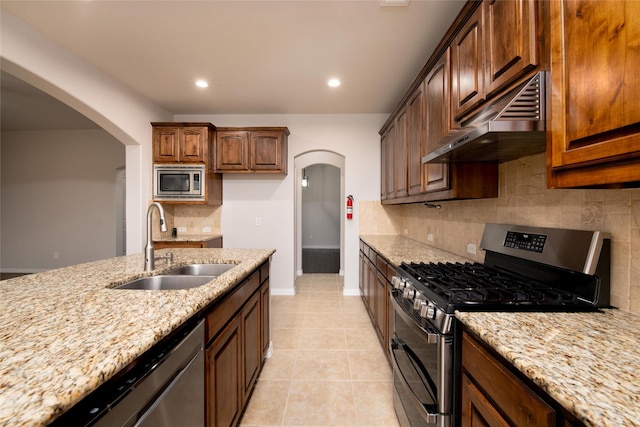 kitchen featuring under cabinet range hood, arched walkways, stainless steel appliances, and a sink