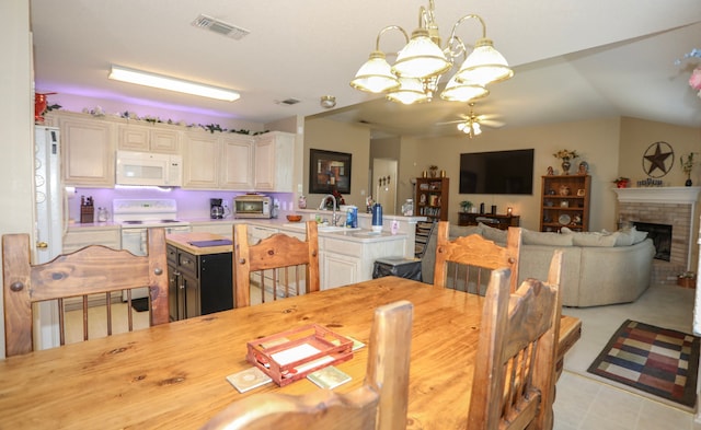 dining room with vaulted ceiling, sink, ceiling fan with notable chandelier, and a brick fireplace