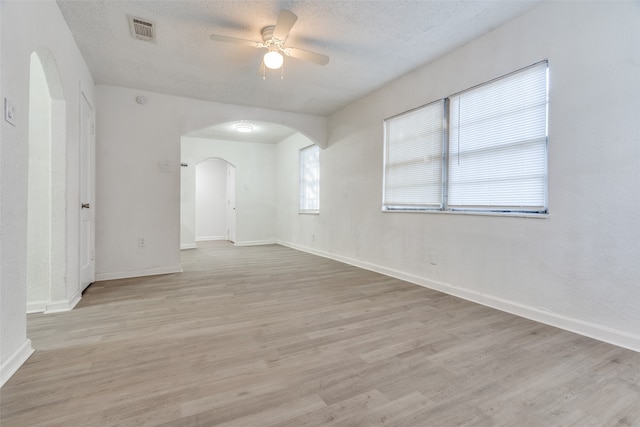 unfurnished room with a textured ceiling, light wood-type flooring, and ceiling fan