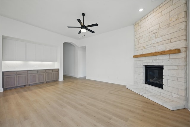 unfurnished living room with a ceiling fan, light wood-type flooring, arched walkways, a fireplace, and baseboards