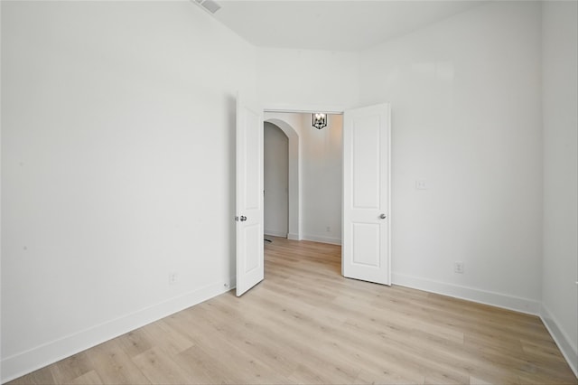 unfurnished room featuring light wood finished floors, baseboards, arched walkways, and visible vents