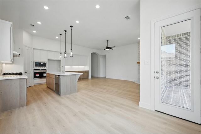 kitchen with a sink, arched walkways, a center island with sink, light countertops, and appliances with stainless steel finishes