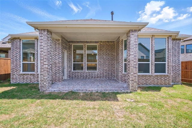 rear view of house featuring brick siding, a yard, and fence