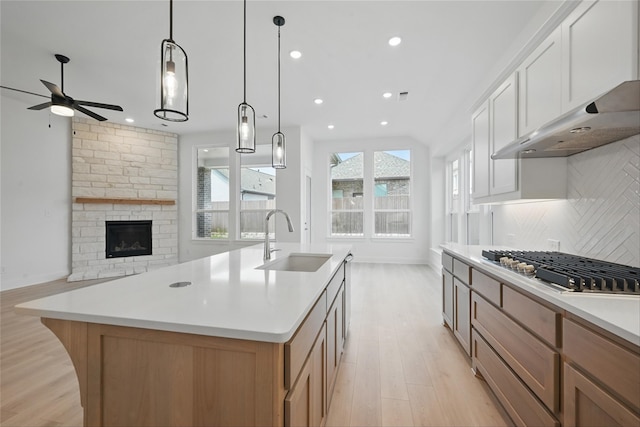 kitchen featuring light wood finished floors, a sink, tasteful backsplash, stainless steel gas stovetop, and ceiling fan