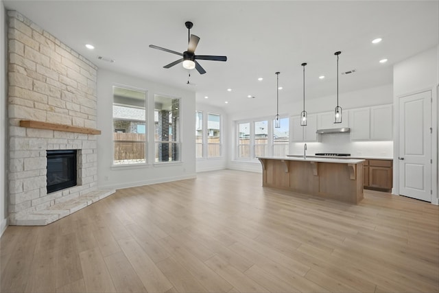 unfurnished living room with a stone fireplace, visible vents, a ceiling fan, a sink, and light wood-style floors