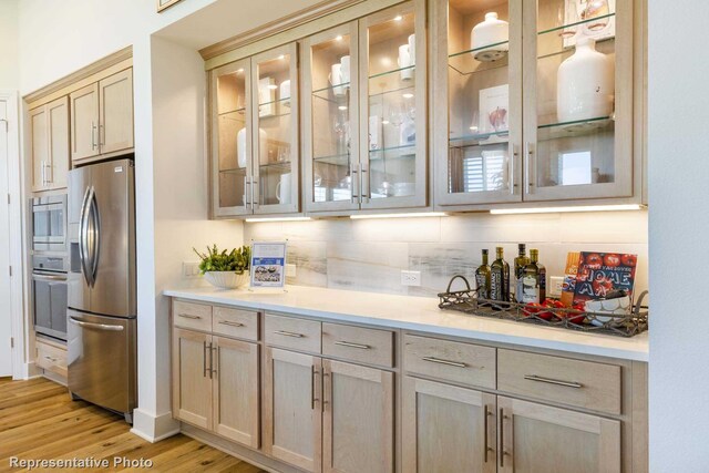 bar with appliances with stainless steel finishes, backsplash, and light hardwood / wood-style floors