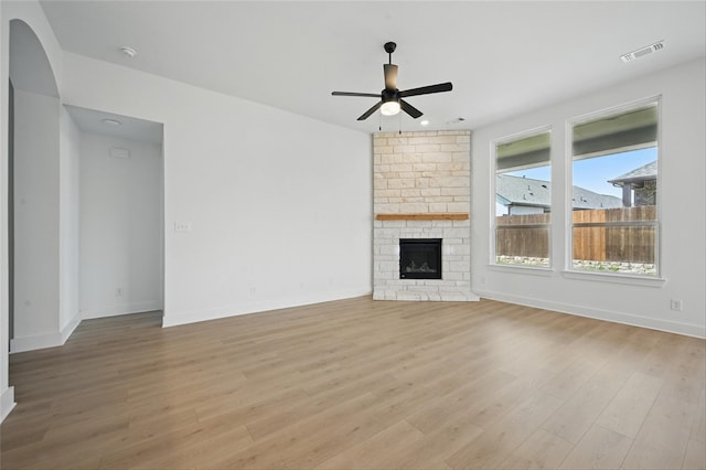 unfurnished living room with light wood-type flooring, ceiling fan, arched walkways, baseboards, and visible vents