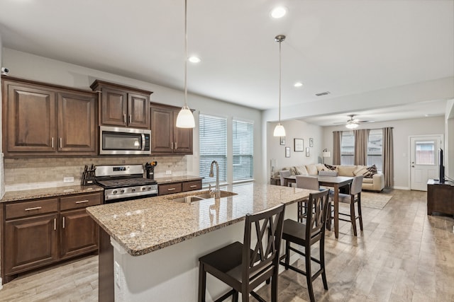 kitchen with a center island with sink, hanging light fixtures, sink, appliances with stainless steel finishes, and light hardwood / wood-style floors