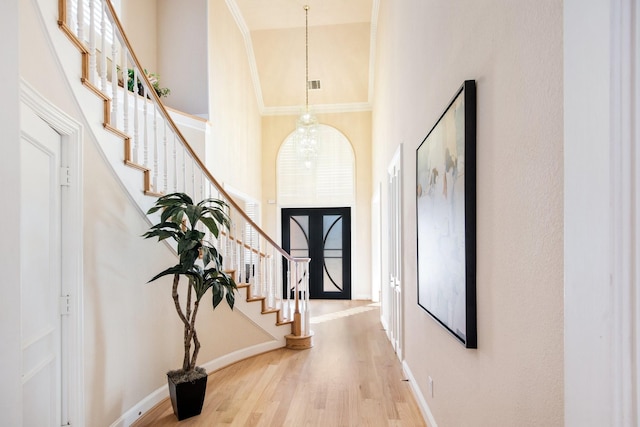 foyer featuring crown molding, a towering ceiling, a notable chandelier, and light wood-type flooring