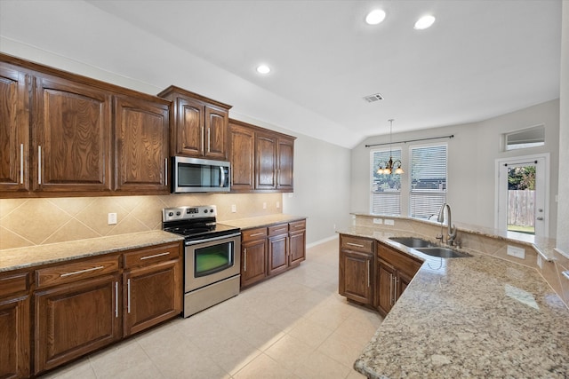 kitchen with sink, an inviting chandelier, light stone counters, pendant lighting, and appliances with stainless steel finishes