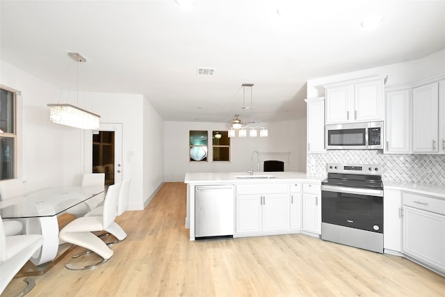 kitchen featuring kitchen peninsula, pendant lighting, stainless steel appliances, and white cabinetry