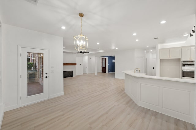 kitchen featuring white cabinets, ceiling fan with notable chandelier, hanging light fixtures, light hardwood / wood-style flooring, and stainless steel double oven