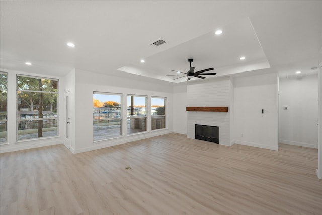 unfurnished living room with a raised ceiling, ceiling fan, a fireplace, and light hardwood / wood-style floors