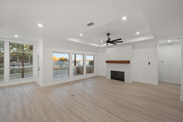 unfurnished living room with a raised ceiling, ceiling fan, a fireplace, and light hardwood / wood-style floors