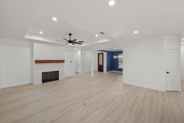 unfurnished living room featuring ceiling fan with notable chandelier, a raised ceiling, a fireplace, and light hardwood / wood-style flooring