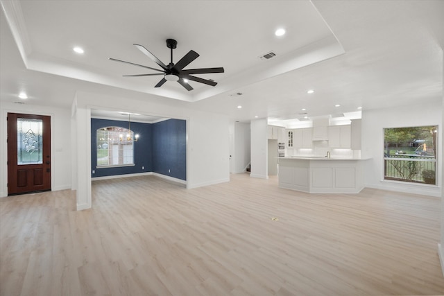 unfurnished living room with light hardwood / wood-style floors, a raised ceiling, and a wealth of natural light