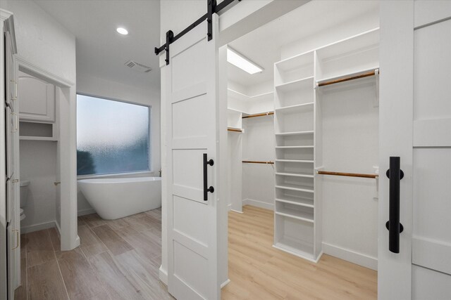 walk in closet with a barn door and light hardwood / wood-style floors