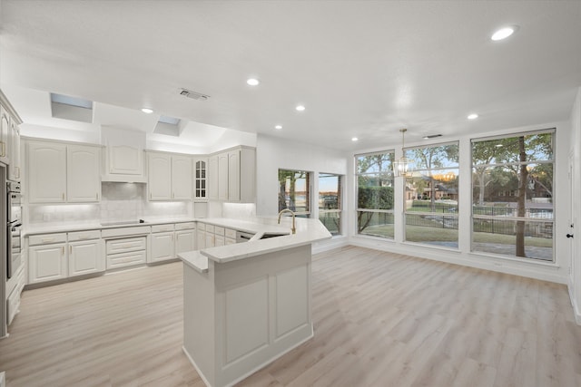 kitchen featuring kitchen peninsula, a chandelier, pendant lighting, decorative backsplash, and light wood-type flooring