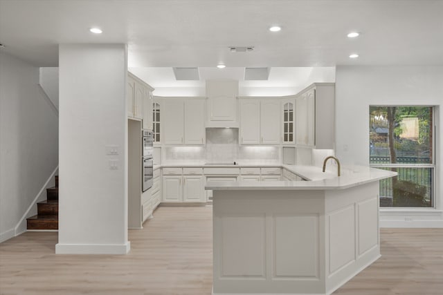 kitchen featuring kitchen peninsula, light hardwood / wood-style flooring, decorative backsplash, double oven, and white cabinetry