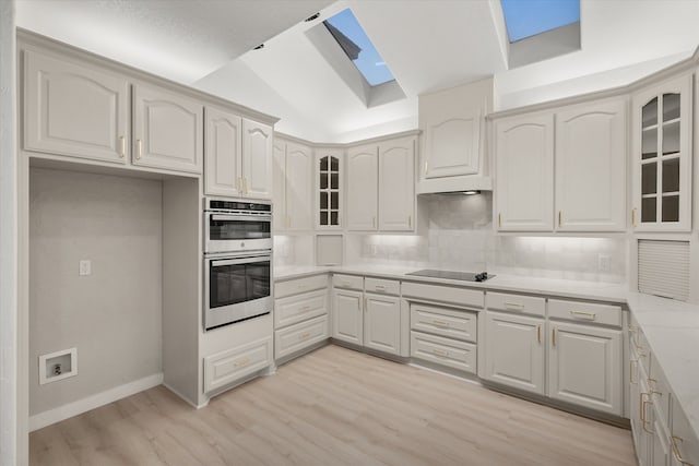 kitchen with tasteful backsplash, vaulted ceiling with skylight, black electric cooktop, double oven, and light hardwood / wood-style flooring