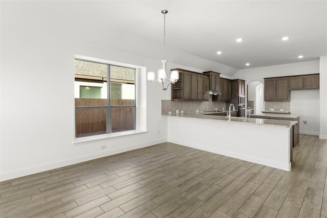 kitchen with kitchen peninsula, tasteful backsplash, light stone counters, dark brown cabinetry, and pendant lighting