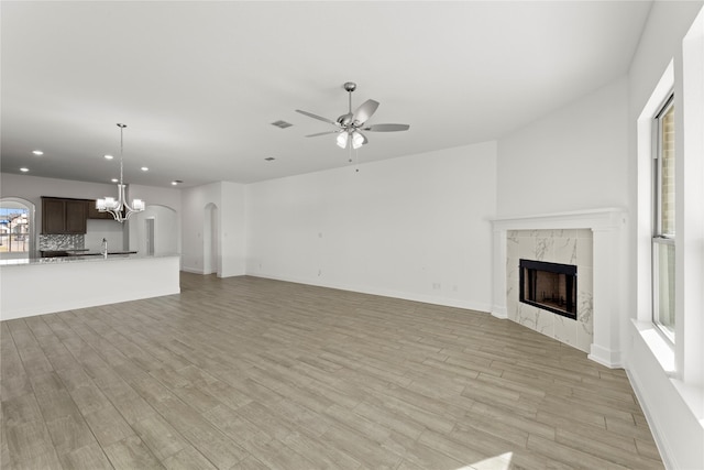 unfurnished living room with ceiling fan with notable chandelier, light hardwood / wood-style floors, and a premium fireplace